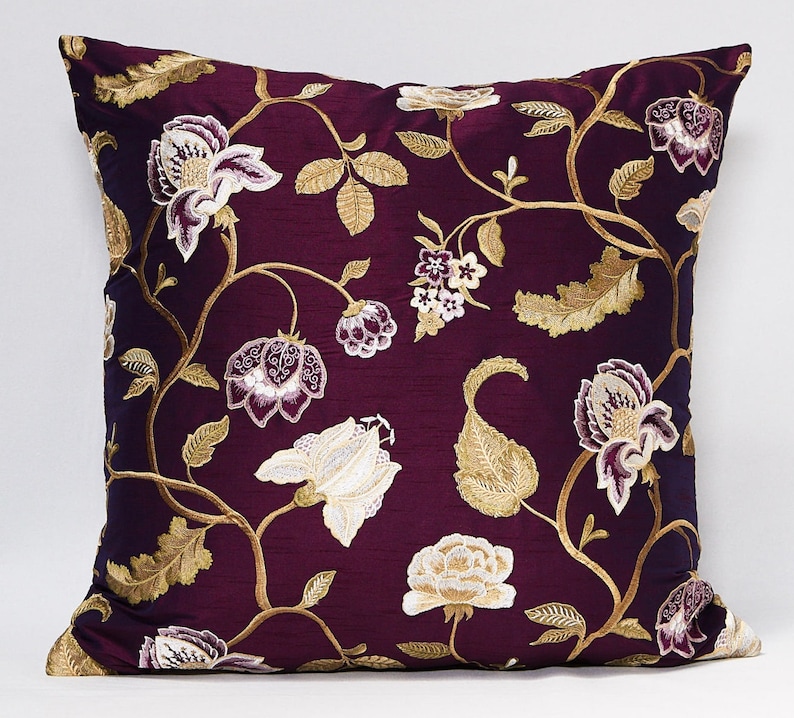 May include: A purple cushion with a floral pattern embroidered in gold and white. The flowers are stylised and have a vintage look.