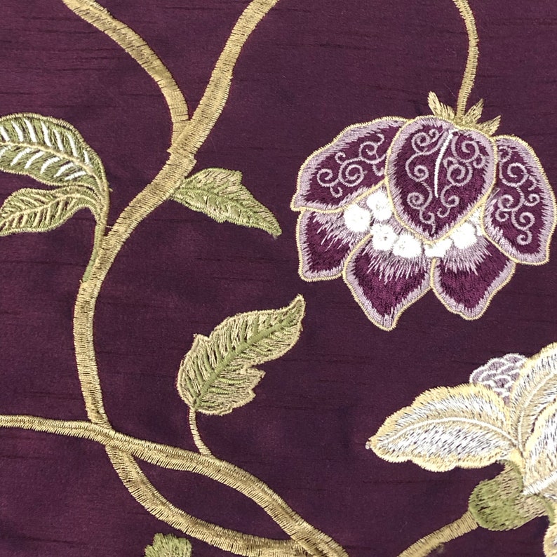 May include: Purple fabric with gold embroidered floral design. The design features a large flower with white accents and smaller leaves.