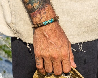 Pode incluir: Um bracelete de madeira castanho com contas turquesa. O bracelete é usado no pulso de uma pessoa com uma tatuagem no braço.
