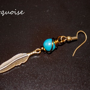 May include: Turquoise blue gemstone bead wrapped in gold wire with a silver feather charm hanging from it. The earring has a gold hook.