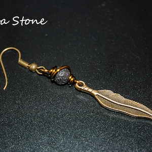May include: A pair of earrings with a black lava stone bead and a gold feather charm. The earrings are made with gold wire and have a hook closure.
