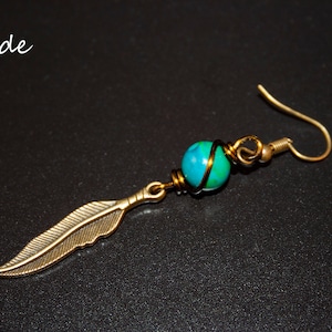 May include: A gold-toned earring with a green and blue jade stone wrapped in wire and a gold-toned feather charm.