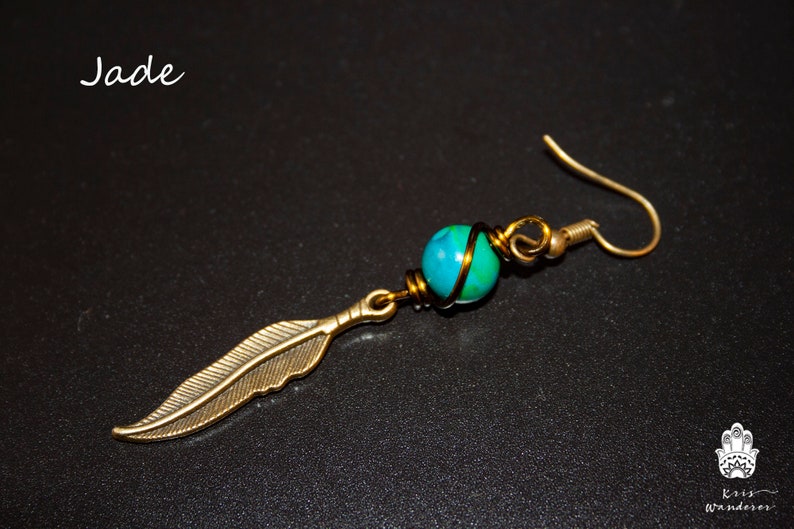 May include: A gold-toned earring with a green and blue jade stone wrapped in wire and a gold-toned feather charm.