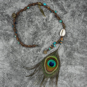 Peut inclure: Un collier en cordon marron avec des perles turquoise et dorées, un pendentif en coquille blanche et une longue plume de paon.