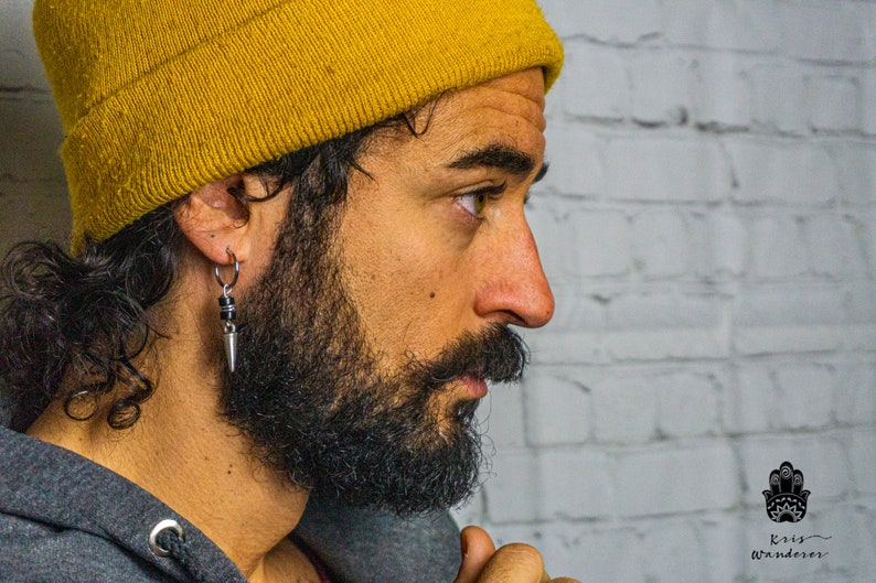 May include: A man with a beard and a yellow beanie is wearing a silver hoop earring with a black bead and a silver spike charm.