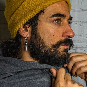 May include: A man with a beard wearing a yellow beanie and a gray hoodie. He is wearing a silver earring with a black bead and a silver spike.