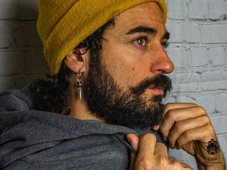 May include: A man with a beard wearing a yellow beanie and a gray hoodie. He is wearing a silver earring with a black bead and a silver spike.