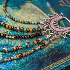 May include: A multi-strand necklace with brown wooden beads, turquoise stones, and silver accents. The necklace features a large, ornate silver pendant with a crescent moon shape.