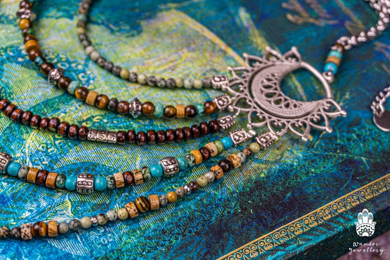 May include: A multi-strand necklace with brown wooden beads, turquoise stones, and silver accents. The necklace features a large, ornate silver pendant with a crescent moon shape.