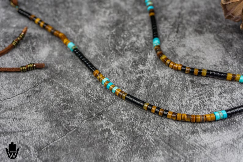 K&ouml;nnte beinhalten: Eine Perlenkette mit schwarzen, braunen und blauen Perlen. Die Kette ist aus nat&uuml;rlichen Steinen gefertigt und hat ein schlichtes Design.