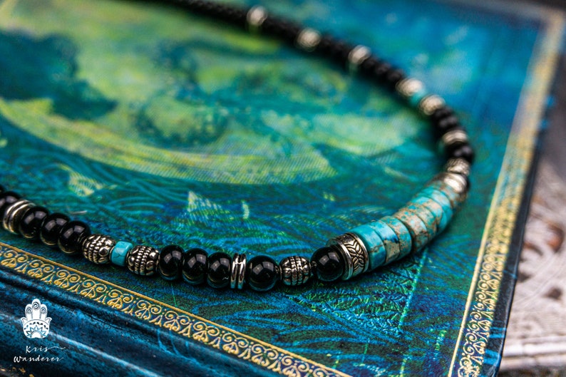 May include: A beaded necklace with black onyx and turquoise stones, accented with silver spacers. The necklace is lying on a blue and green patterned surface.