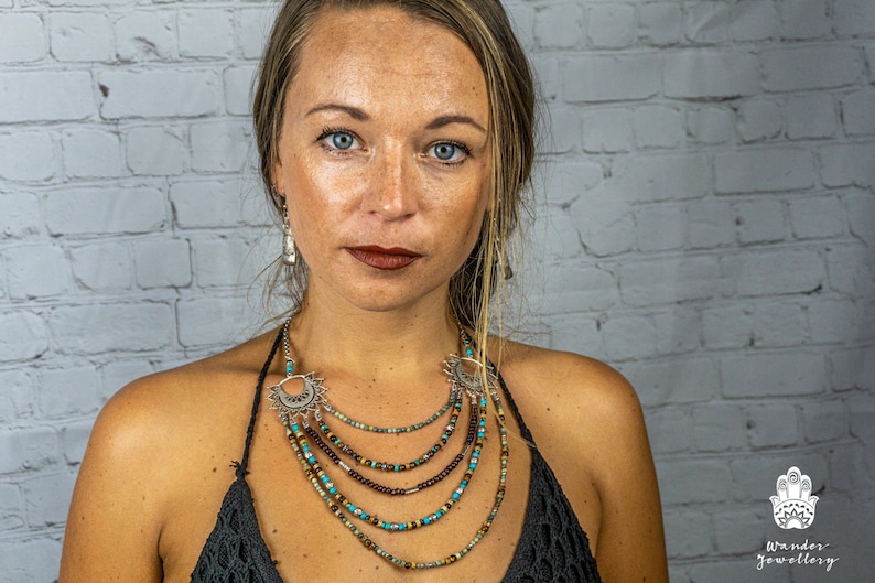 May include: A woman wearing a layered necklace with turquoise and brown beads and silver accents. The necklace has a crescent moon pendant. The woman is wearing a black top and has long brown hair.