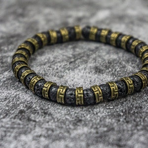 May include: A black lava rock bracelet with gold-toned metal beads. Each bead features a geometric pattern.