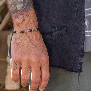 Op de afbeelding: Een zwarte kralen armband met een zilveren ketting om de pols.