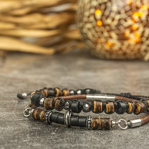 Puede incluir: Dos pulseras con cuentas de madera marrón y negra y detalles plateados. Las pulseras están sobre una superficie gris.