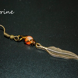 May include: Citrine gemstone dangle earring with a gold-toned wire wrapped around the stone and a feather charm. The earring has a gold-toned hook.