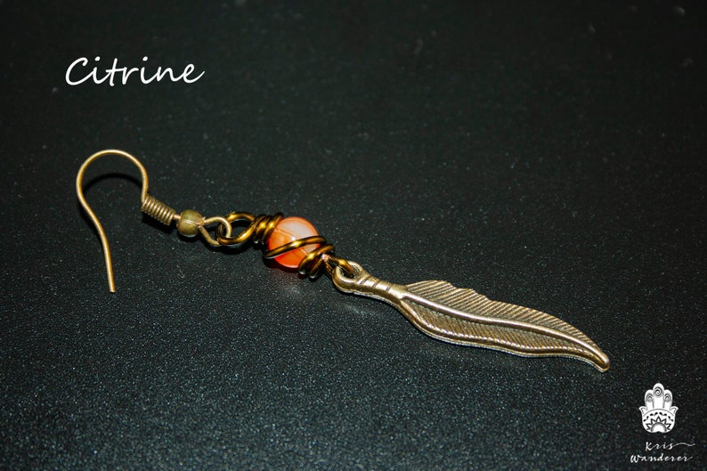 May include: Citrine gemstone dangle earring with a gold-toned wire wrapped around the stone and a feather charm. The earring has a gold-toned hook.