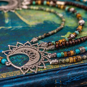 May include: A multi-strand necklace with brown wooden beads, turquoise beads, and silver accents. The necklace features a large, ornate silver pendant in the shape of a crescent moon.