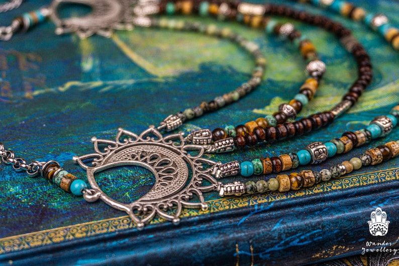May include: A multi-strand necklace with brown wooden beads, turquoise beads, and silver accents. The necklace features a large, ornate silver pendant in the shape of a crescent moon.