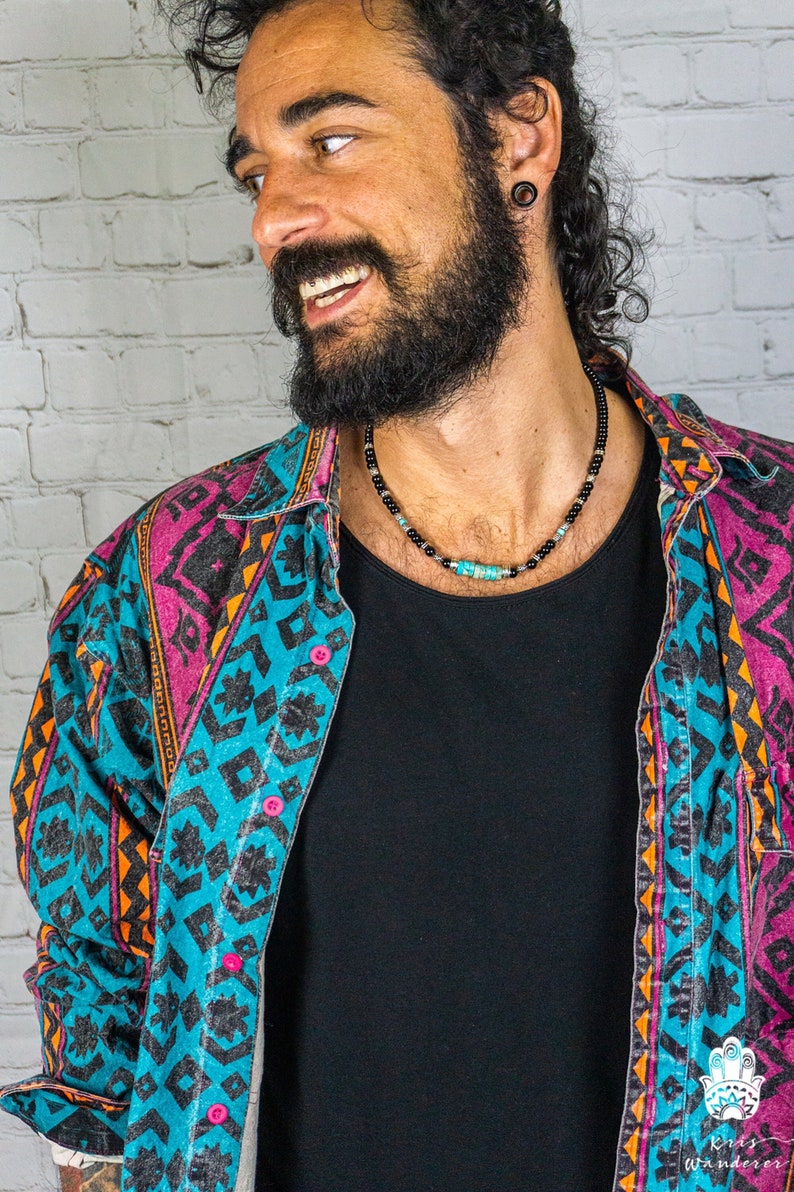 May include: A man wearing a blue, pink, and orange patterned shirt with a black beaded necklace with turquoise accents.