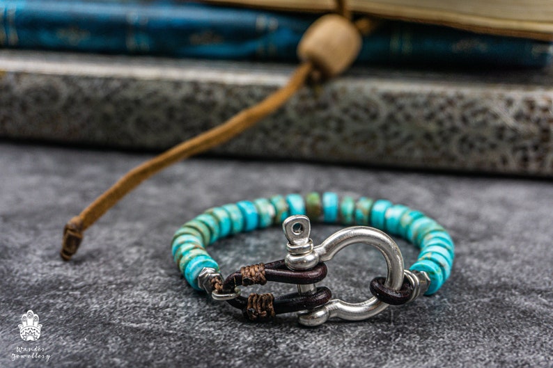Op de afbeelding: Een turquoise en zilveren armband met een leren sluiting. De armband is gemaakt van kleine, ronde kralen en heeft een zilveren togglesluiting.