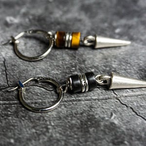 May include: A pair of silver hoop earrings with a silver spike and a black or tiger's eye bead dangle.
