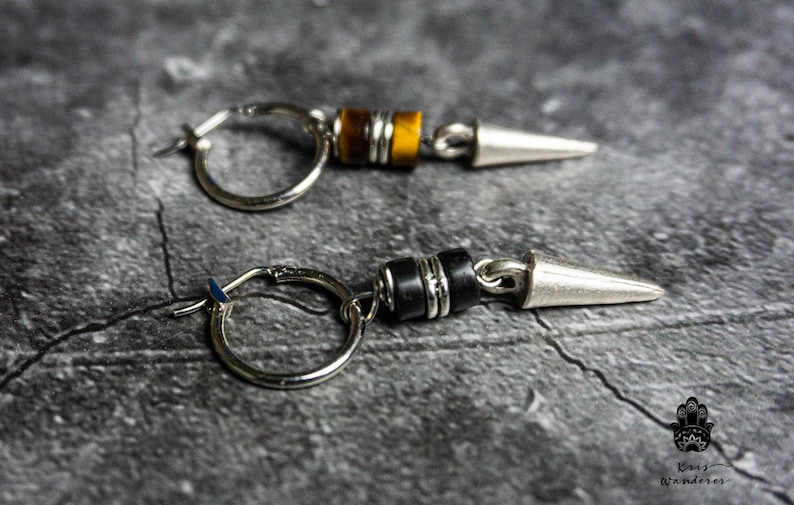 May include: A pair of silver hoop earrings with a silver spike and a black or tiger's eye bead dangle.