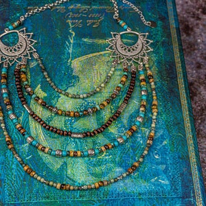 May include: Multi-strand necklace with turquoise, brown, and gold beads. The necklace features a silver pendant with a decorative design.