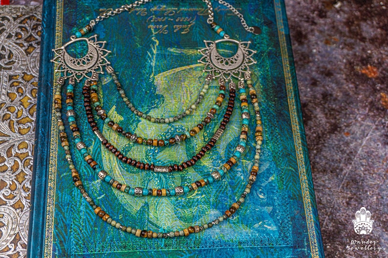May include: Multi-strand necklace with turquoise, brown, and gold beads. The necklace features a silver pendant with a decorative design.