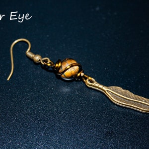 May include: A gold-toned earring with a tiger's eye stone wrapped in wire and a feather charm.