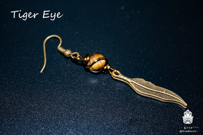 May include: A gold-toned earring with a tiger's eye stone wrapped in wire and a feather charm.