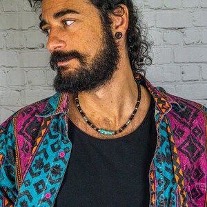 May include: A close-up of a man wearing a colorful patterned shirt and a black beaded necklace with turquoise accents.