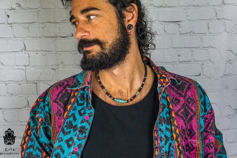 May include: A close-up of a man wearing a colorful patterned shirt and a black beaded necklace with turquoise accents.