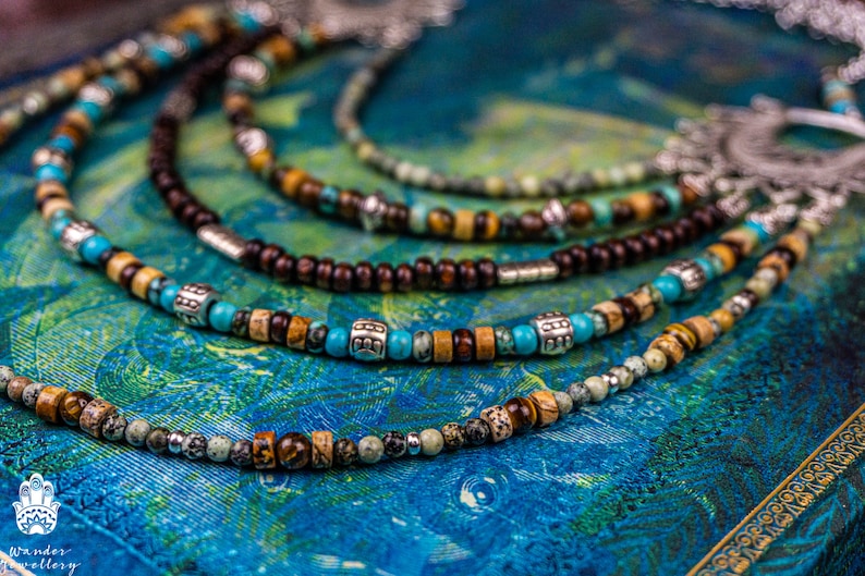 May include: A multi-strand necklace with brown wooden beads, turquoise beads, and silver accents. The necklace is on a blue and green patterned surface.