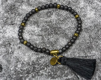 May include: Black lava rock beaded bracelet with gold accents and a black tassel.
