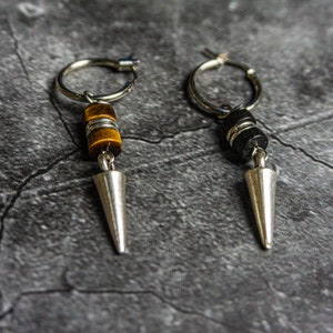 May include: A pair of silver hoop earrings with a silver spike charm. One earring has a tiger's eye stone bead and the other has a black stone bead.