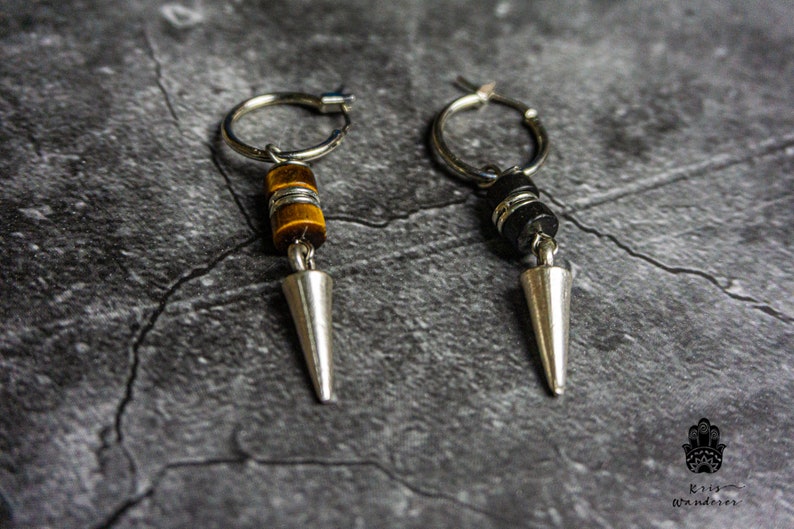 May include: A pair of silver hoop earrings with a silver spike charm. One earring has a tiger's eye stone bead and the other has a black stone bead.