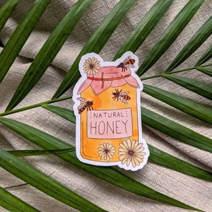Peut inclure: Un autocollant repr&eacute;sentant un pot de miel avec un couvercle rose et une &eacute;tiquette indiquant "NATURAL HONEY". Le pot est entour&eacute; d'abeilles et de fleurs.