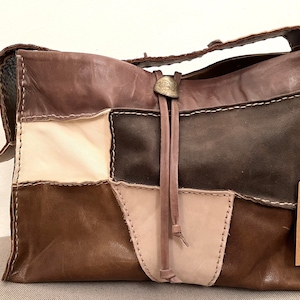 May include: A brown leather patchwork tote bag with a long brown leather strap and a metal accent. The bag has a tag that reads "Unique Handmade Bags Made one by one with natural and pretty natural leather as cotton."