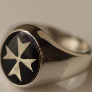 Puede incluir: Un anillo de plata con una incrustación de esmalte negro que presenta una cruz blanca de Malta.