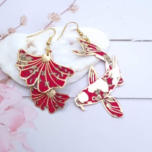 Könnte beinhalten: Ein Paar goldene Ohrringe mit einem roten und weißen Blumenmuster. Ein Ohrring zeigt ein Koi-Fisch-Design, während der andere ein doppelschichtiges Fächer-Design zeigt.