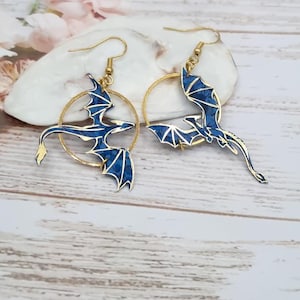 May include: A pair of gold hoop earrings with blue dragon charms. The dragons are detailed with gold accents and have a textured blue finish.