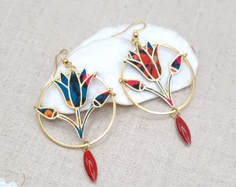Pode incluir: Um par de brincos de argola dourados com um design floral. Os brincos apresentam uma flor azul e vermelha com um pingente de lágrima vermelho.