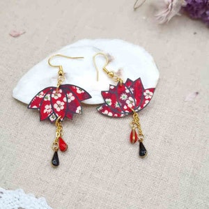 May include: Red and white floral patterned earrings with gold chains and black and red beads hanging from them.