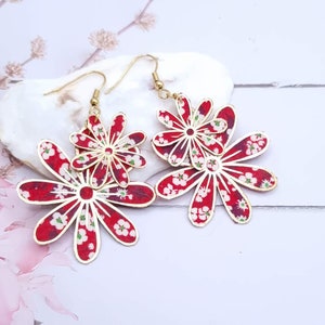 Könnte beinhalten: Rote und weiße Blumenmuster-Ohrringe mit goldenen Akzenten. Die Ohrringe bestehen aus übereinanderliegenden Papierblumen.