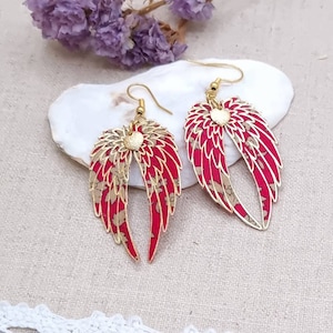 May include: A pair of gold-colored wing-shaped earrings with red and tan floral patterned wings. The earrings have a gold-colored heart-shaped accent in the center and gold-colored ear hooks. The earrings are displayed on a white surface.