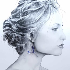 May include: A woman with her hair styled in a bun is wearing a pair of silver earrings with a blue and black dragon design.