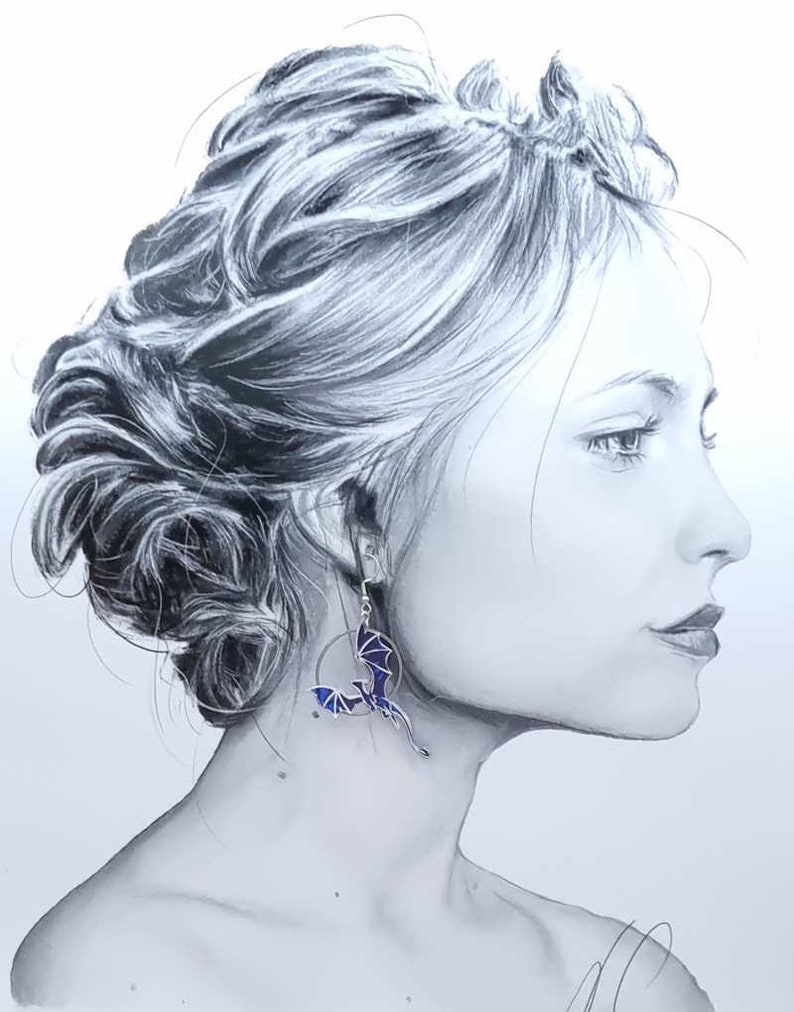 May include: A woman with her hair styled in a bun is wearing a pair of silver earrings with a blue and black dragon design.