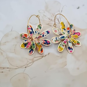 Peut inclure: Une paire de boucles d'oreilles créoles dorées avec un motif floral. Les fleurs sont en tissu et présentent un motif multicolore. Ces boucles d'oreilles sont une pièce forte et seraient parfaites pour une fête d'été.