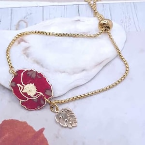 May include: Gold-coloured adjustable bracelet with a red poppy flower charm and a gold leaf charm. The bracelet has a delicate chain and a sliding bead for adjustment. The poppy charm has gold detailing.